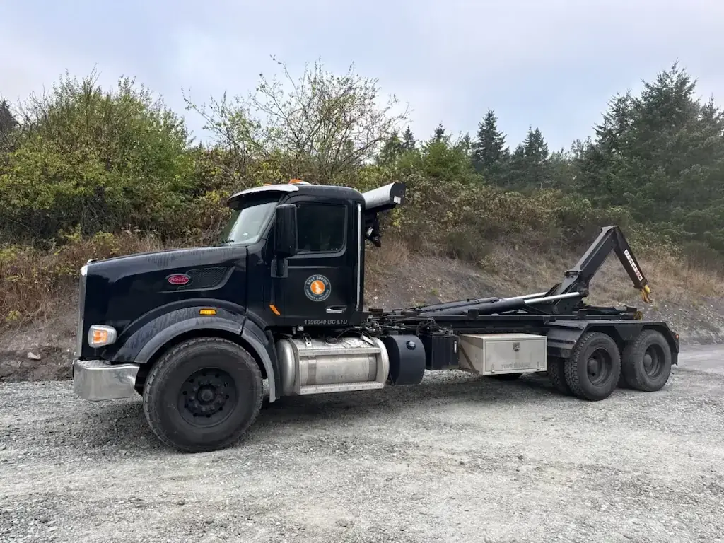 Black Salt Spring Garbage & Recycling Peterbilt hook-lift truck with the company decal, parked on gravel