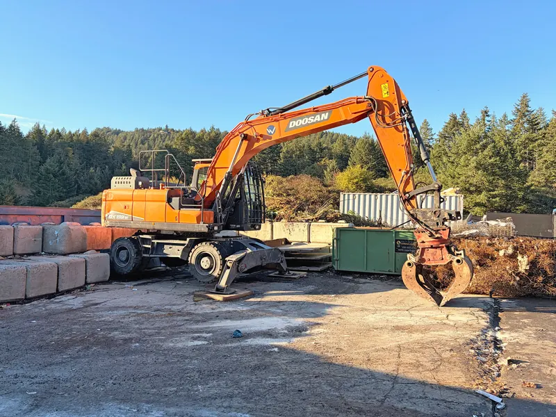 Doosan material handler with a grapple sorting material in the yard