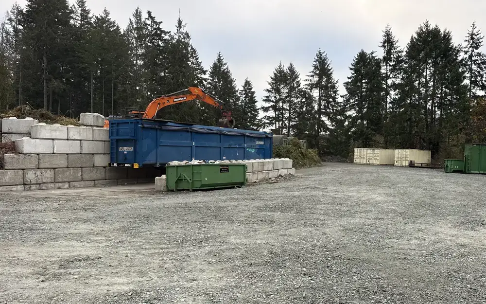 Salt Spring Garbage drop-off yard with an orange excavator loading a blue bin, and green rental bins